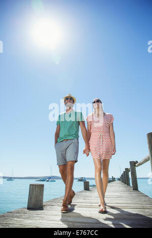 Couple holding hands walking along wooden dock Banque D'Images