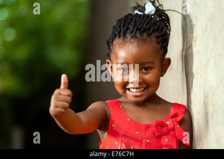 Portrait of happy little African girl doing Thumbs up sign en plein air. Banque D'Images