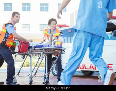 Les ambulanciers wheeling patient dans le stationnement de l'hôpital Banque D'Images