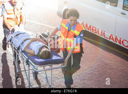 Les ambulanciers wheeling patient dans le stationnement de l'hôpital Banque D'Images