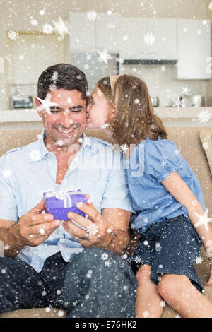 Image composite de girl kissing father holding gift box sur canapé Banque D'Images