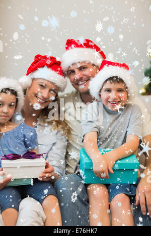 Image composite de famille dans christmas hat holding presents sur canapé Banque D'Images