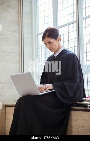 Assis sur un banc juge using laptop in courthouse Banque D'Images