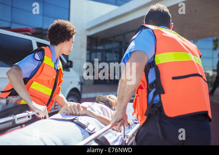 Les ambulanciers wheeling patient dans le stationnement de l'hôpital Banque D'Images