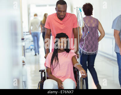 Man wheeling girlfriend in hospital hallway Banque D'Images