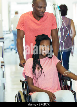 Man wheeling girlfriend in hospital hallway Banque D'Images
