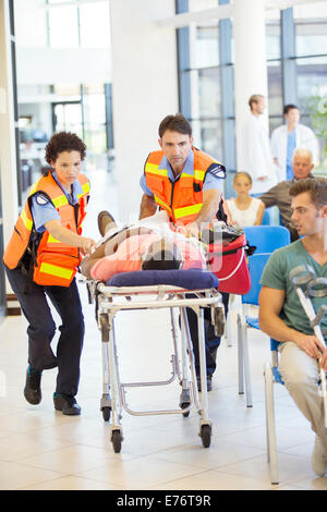 Les ambulanciers wheeling patient in hospital Banque D'Images