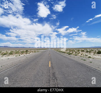 Une route du désert vide traverse le Nevada à l'horizon sous un ciel bleu nuageux Banque D'Images
