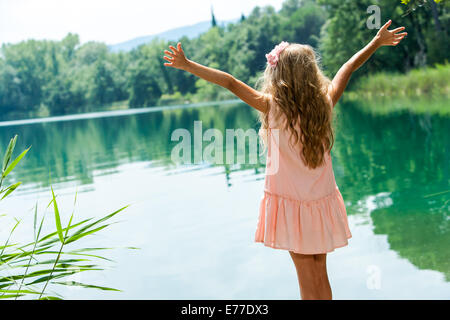 Jeune fille en robe rose debout les bras ouverts au bord du lac. Banque D'Images