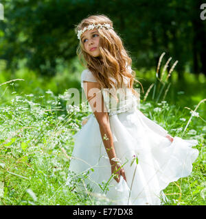 Cute girl holding white dress in green field. Banque D'Images