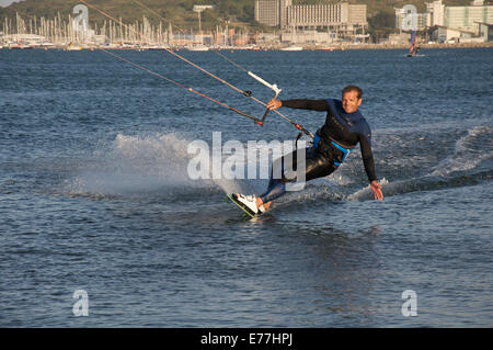 Sports d'eau. Male kiteboarder, porter une combinaison isothermique, excès de vitesse à travers l'eau du port de Portland, dans le Dorset, Angleterre, Royaume-Uni. Banque D'Images