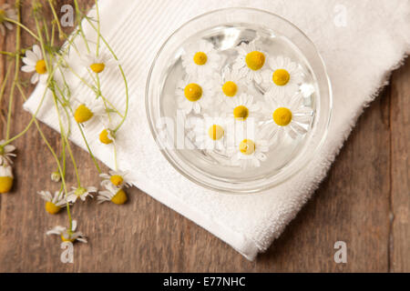 La camomille dans l'eau sur la serviette blanche sur table en bois Banque D'Images