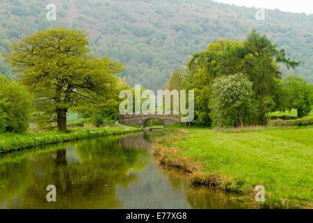 Anglais pittoresque paysage rural, de chênes et de pont en arc reflète dans la surface miroir de stream à travers champs au pied de la colline boisée Banque D'Images