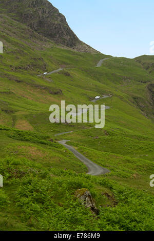 Vue sur route étroite et raide menant au sommet du Hardknott Pass en Cumbria serpentant à travers le paysage vert anglais de montagnes sans arbres voilés Banque D'Images