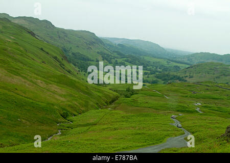 Vue de Hardknott Pass, route étroite serpentant à travers les vallées d'émeraude de l'Anglaise, cours d'eau méandrique, bois, et les montagnes de Lake District. Banque D'Images