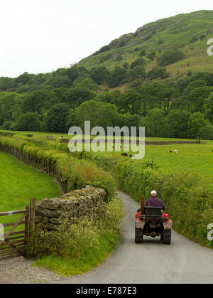 English paysage rural avec le fermier sur quad de la conduite sur route étroite bordée de haies et bordée par des champs verts et côtes Banque D'Images