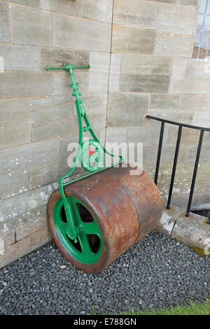 Vieille pelle avec rusty metal drum / rouleau et poignée vert leaning against wall Banque D'Images