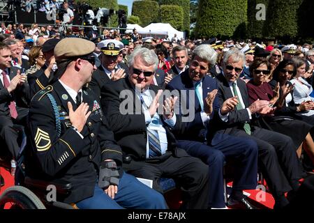 US Army Ranger Sgt. Cory Remsburg Première Classe est applaudie par son père Craig Remsburg, Secrétaire d'État John Kerry, et le ministre de la Défense Chuck Hagel lors d'observations du Président Barack Obama à la 70e Commémoration franco-américaines D-Day Cérémonie au cimetière américain de Normandie le 6 juin 2014 à Colleville-sur-Mer, France. Banque D'Images