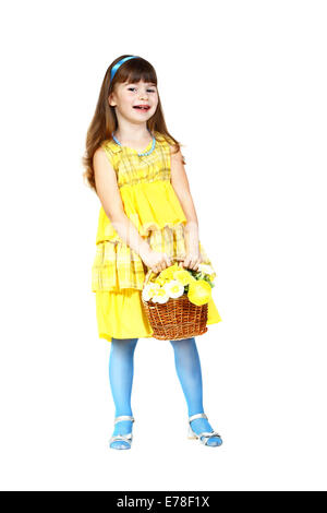 Jolie petite fille en robe jaune et bleu avec panier de fleurs dans les mains ressemble malicieusement. Portrait pleine hauteur isolated on white Banque D'Images