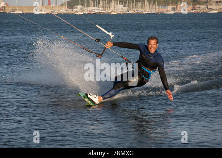 Sports d'eau. Male kiteboarder, porter une combinaison isothermique, excès de vitesse à travers l'eau du port de Portland, dans le Dorset, Angleterre, Royaume-Uni. Banque D'Images