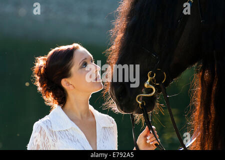 Jeune femme tenant un cheval frison noir, rétroéclairé, le nord du Tyrol, Autriche Banque D'Images