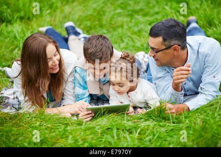 Heureuse famille des quatre allongé sur l'herbe avec touchpad Banque D'Images