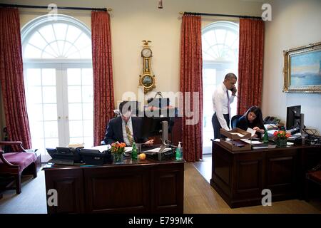 Le président américain Barack Obama parle au téléphone comme Brian Mosteller, Directeur des opérations du Bureau ovale et Ferial Govashiri, Assistant personnel du Président, le travail dans l'avant-Bureau ovale de la Maison Blanche le 12 juin 2014 à Washington, DC. Banque D'Images