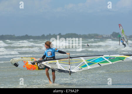Man carrying windsurfer en mer agitée à West Wittering Beach, West Wittering, Chichester, West Sussex, Angleterre Banque D'Images