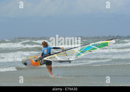 Man carrying windsurfer en mer agitée à West Wittering Beach, West Wittering, Chichester, West Sussex, Angleterre Banque D'Images