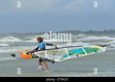 Man carrying windsurfer en mer agitée à West Wittering Beach, West Wittering, Chichester, West Sussex, Angleterre Banque D'Images