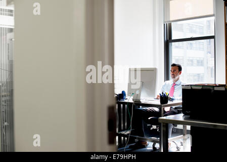 Un homme assis dans un bureau à l'aide d'un ordinateur. Banque D'Images