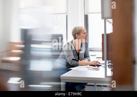 Une femme travaillant dans un bureau à son bureau, à l'aide d'une souris d'ordinateur. Banque D'Images