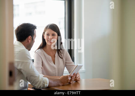 Un homme et une femme dans un bureau, le partage d'une tablette numérique. Banque D'Images