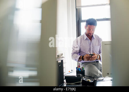 La vie de bureau. Un homme contrôler son téléphone dans un bureau. Banque D'Images