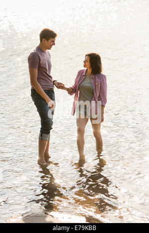 Un couple holding hands, pagayer en eau peu profonde au bord du lac. Banque D'Images