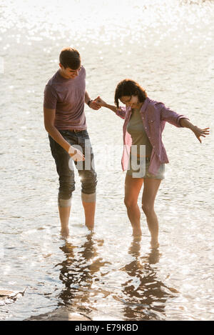 Un couple holding hands, pagayer en eau peu profonde au bord du lac. Banque D'Images