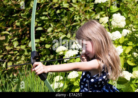 Peu caucasian girl visant flèche de big bow sur fond vert jardin piscine en plein air Banque D'Images