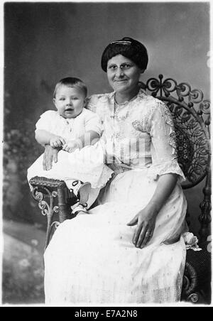 Smiling Woman Wearing Eyeglasses avec Happy bébé sur le bras du fauteuil en osier, Portrait, vers 1920 Banque D'Images