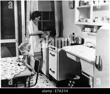 Woman Cooking in Kitchen avec Young Boy Eating Cookies avec du lait, aux États-Unis, vers 1955, à partir du film documentaire, "Emerging femme', Women's Film Project, 1974 Banque D'Images