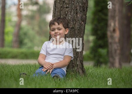 Portrait of cute boy relaxing contre tree in park Banque D'Images