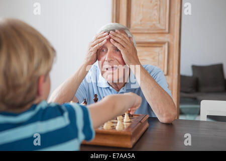 Choqué senior man with head in hands à à grandson tout en jouant aux échecs à la maison Banque D'Images