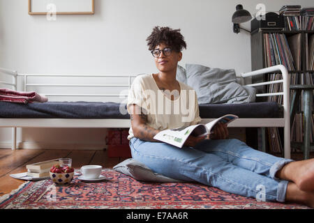 Young woman reading magazine dans la chambre Banque D'Images