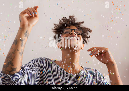 Happy young woman enjoying confettis tombant sur son sur fond gris Banque D'Images