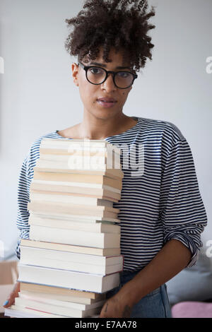 Portrait of young woman carrying pile de livres à la maison Banque D'Images