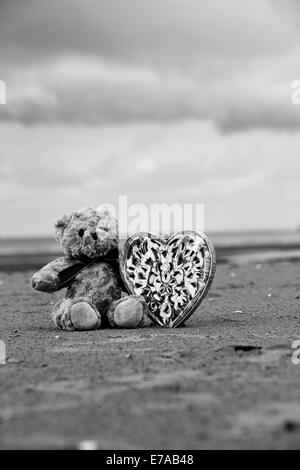 Noir et blanc, ours en peluche sur la plage avec un coeur en bois Banque D'Images