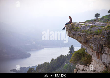 Jeune homme assis sur le bord de la falaise et à la rivière au-dessous Banque D'Images