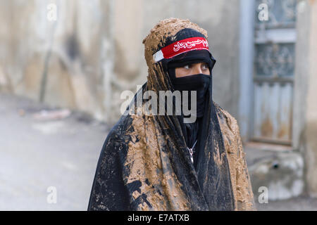 Jeune femme musulmane chiite, vêtu d'un tchador noir couvert de boue, de deuil pendant le jour de l'Achoura dans Bijar, Iran. Banque D'Images