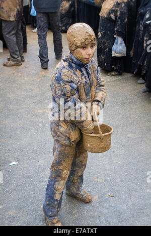 Jeune garçon musulman chiite, couvert de boue, transportant un panier avec plus de boue, le jour de l'Achoura, dans Bijar, Iran. Banque D'Images