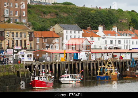 Bateaux de pêche colorés amarrés dans le port de Whitby avec des bâtiments de mer maison de ville anglais regroupés le long du quai Banque D'Images