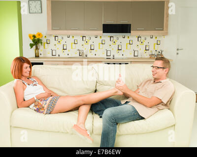 Young caucasian woman relaxing on sofa, man giving pied masssage à sa petite amie Banque D'Images